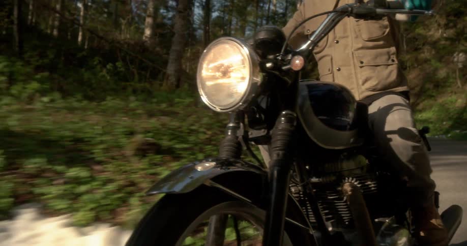 A man rides his motorcycle past the hills and trees