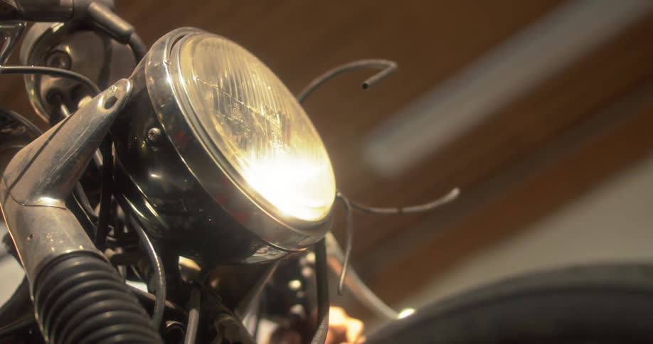 A vintage motorcycles headlight illuminates the darkness casting a warm glow