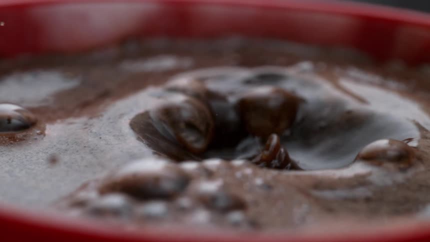A single droplet falls into a red cup filled with coffee