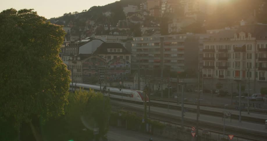 Train passing through an urban city with the suns reflection in the background