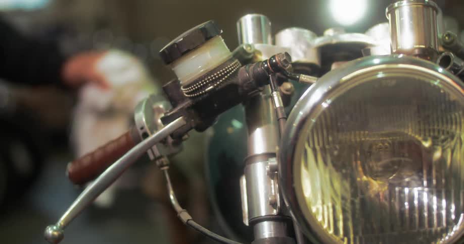 A motorcycle with a big round headlight and then a person in a black coat arrives and grabs the handlebars