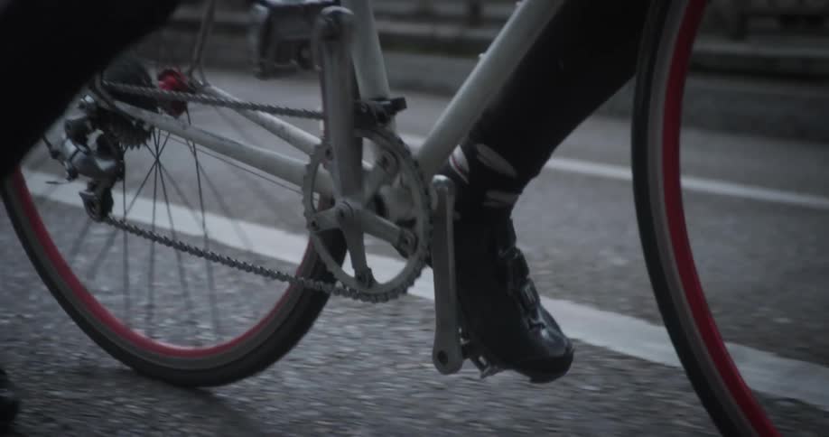 Legs of a person starting to ride a bicycle on a paved road