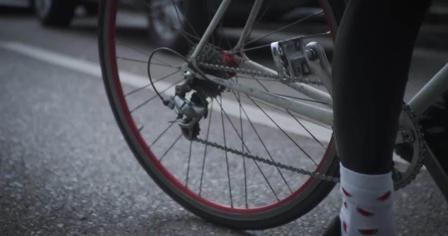A cyclist in a blue shirt riding her bike on an asphalt street and then she stops and puts her feet on the ground