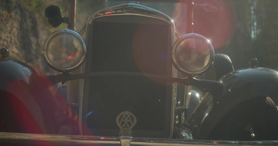 A vintage car gleams in the sunlight its chrome headlights and emblem reflecting the warmth