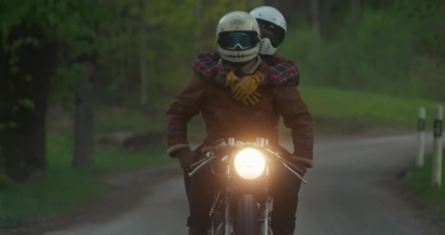 Two people hugging each other riding a motorcycle on a narrow natural road