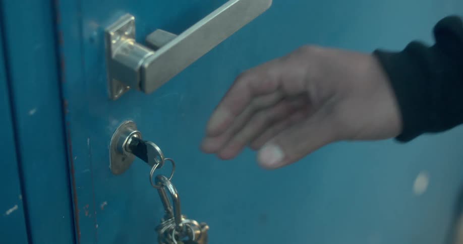 A mans hand is shown unlocking and opening a blue door