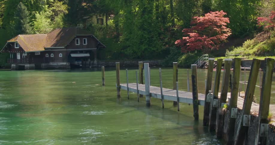 A lake with greenish water and a wooden pier in front and on the edge of the lake there is a large wooden house