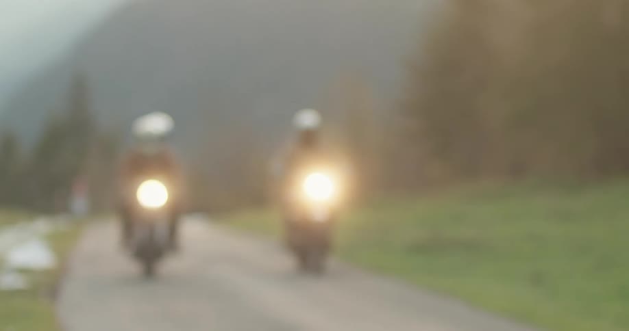 People in helmets on two motorcycles on a narrow road