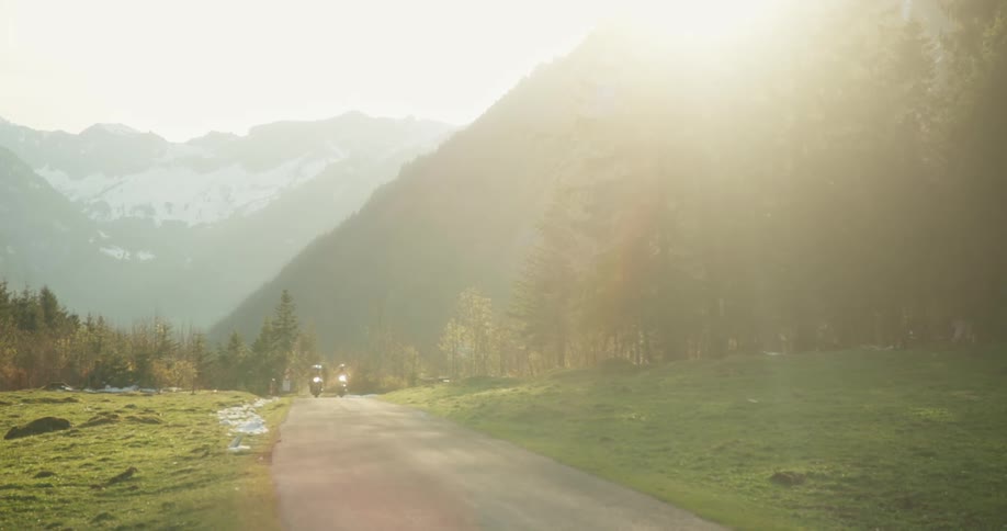 Two motorcycles passing through a narrow road surrounded by mountains