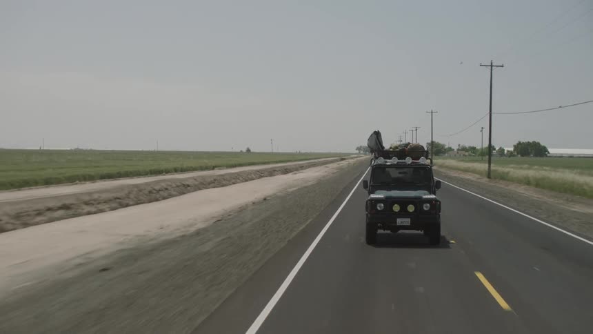 Jeep driving down a two-lane highway with luggage on top