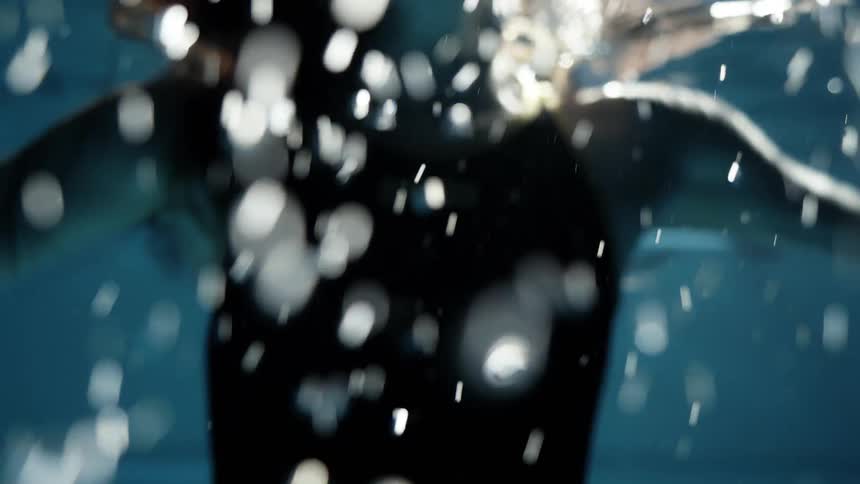A woman in a swimsuit dives into the water sending droplets flying in all directions