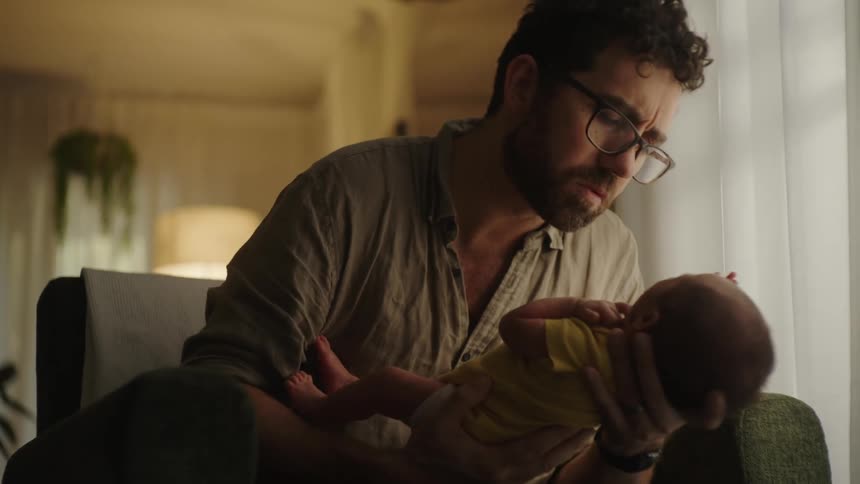 Father sitting in an armchair giving his newborn baby a kiss