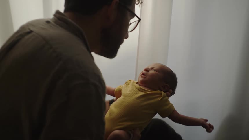 Father holding a crying baby leans down to kiss the child
