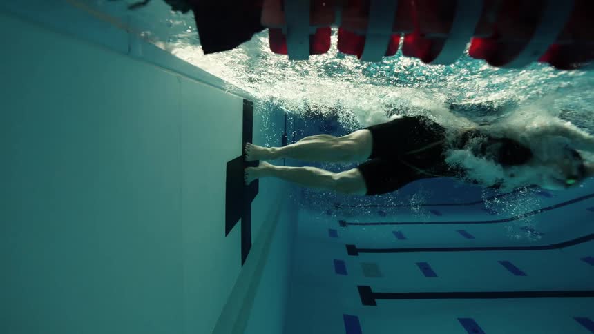 Legs of a woman swimming in a pool and transitioning on the wall