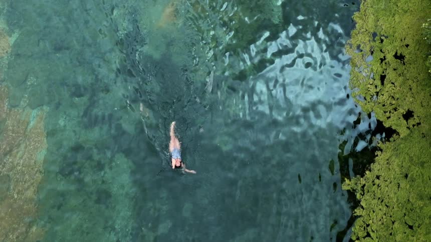 Overhead view of a woman in a swimsuit swimming on her back in a lake