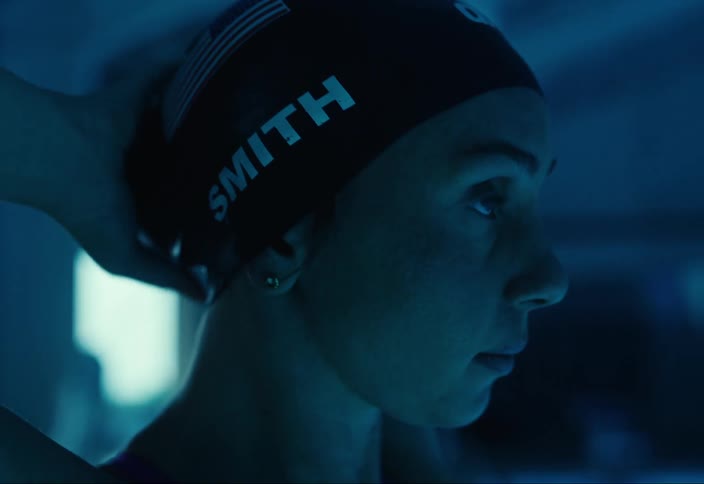A woman is adjusting a swim cap in a dimly lit bluetoned environment