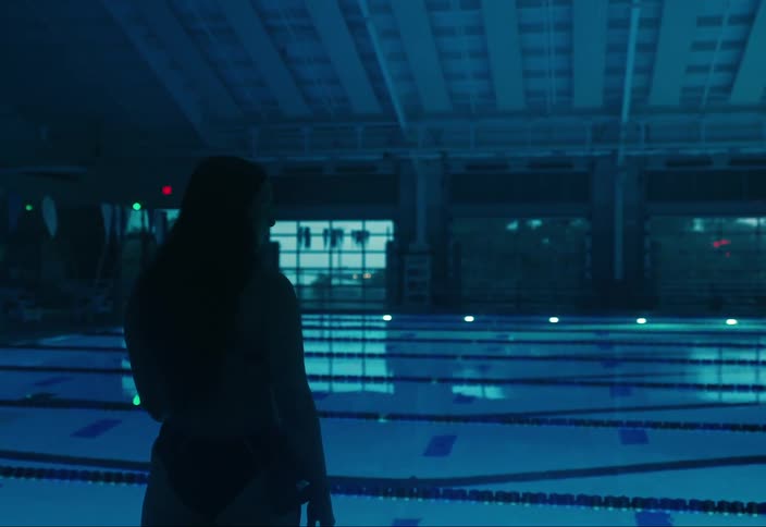 Woman in swimsuit facing a pool with swimming lanes