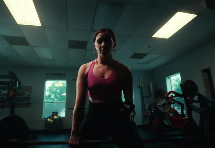 A young woman is standing and lifting a barbell in a gym