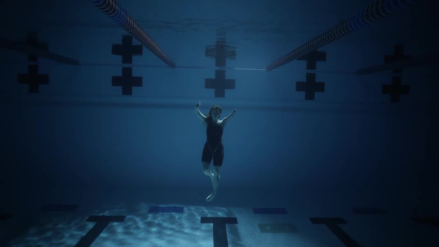 A woman is floating underwater in the pool