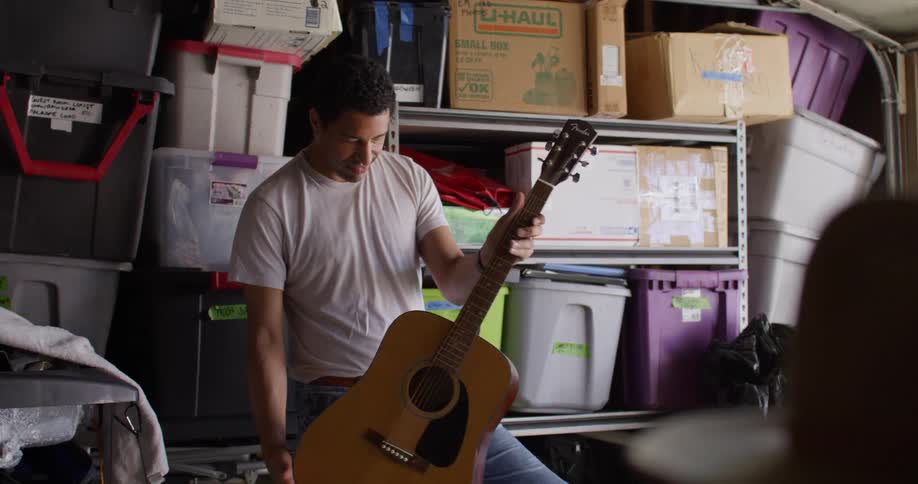 Man standing in a garage smiles while examining a guitar