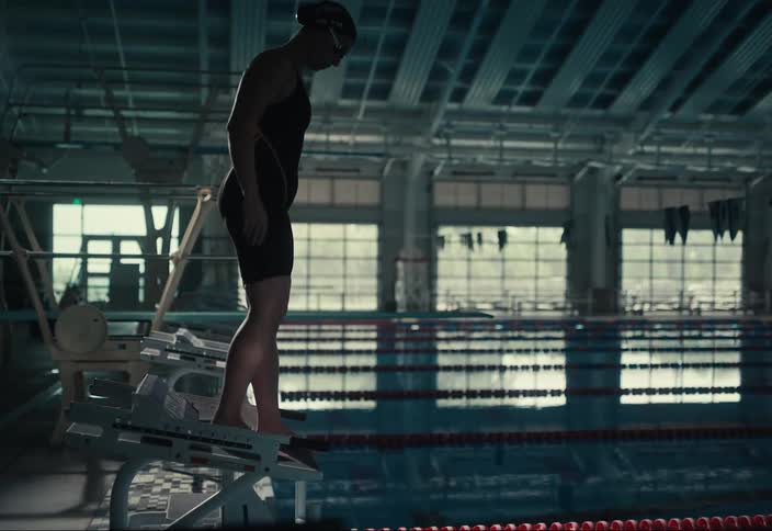 Woman in swimming costume climbing onto platform and jumping into pool