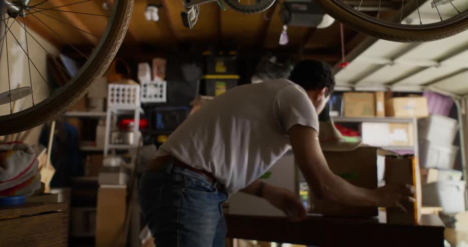 Man in a garage taking boxes out and putting them on a table and putting others away