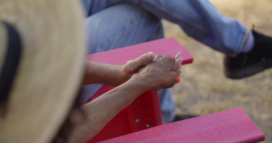 Man and woman sitting outdoors on wooden chairs hold hands