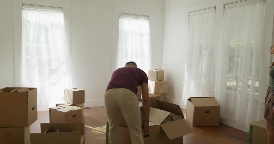 A man and a woman enter an empty room filled with boxes each carrying their own