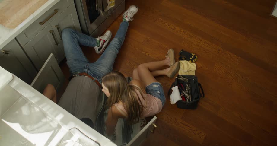 Woman lying down handing a tool to a man who is also lying down under a sink