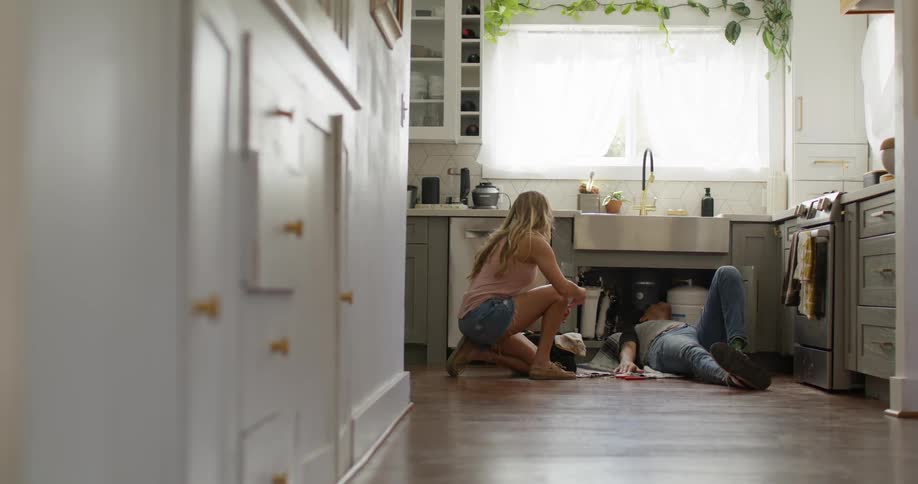 Woman handing a tool to a man who is fixing the kitchen sink