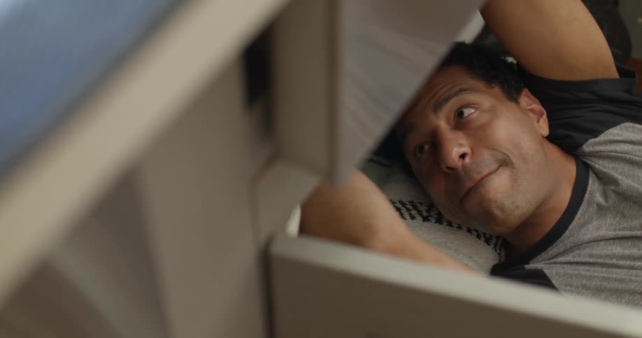A closeup of a man lying on the floor fixing a sink at home