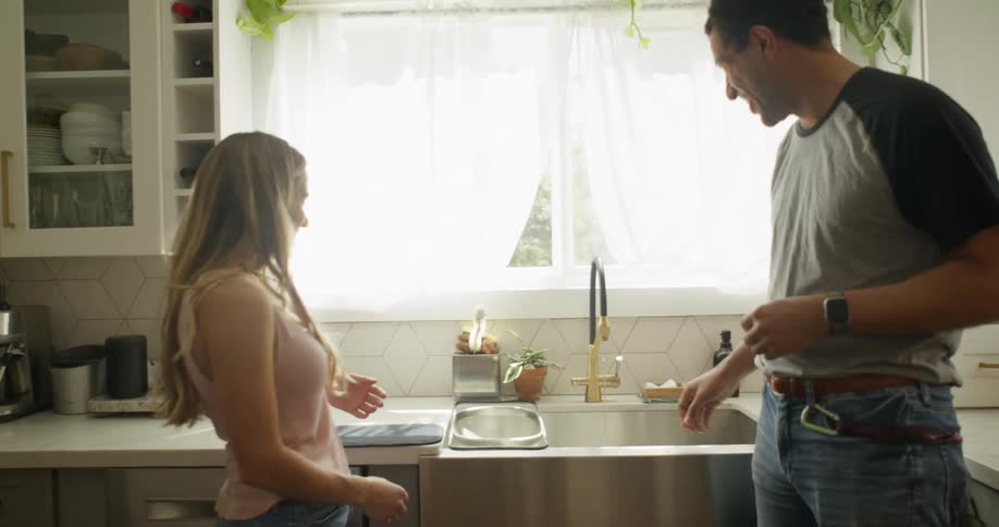 Man throwing water at a woman from the sink tap and they both laugh
