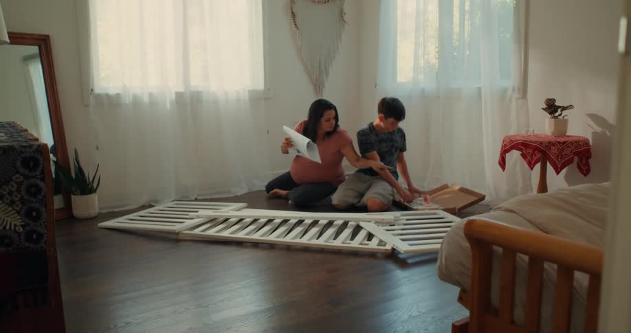 Pregnant mother sitting next to her son reading a manual for assembling a crib