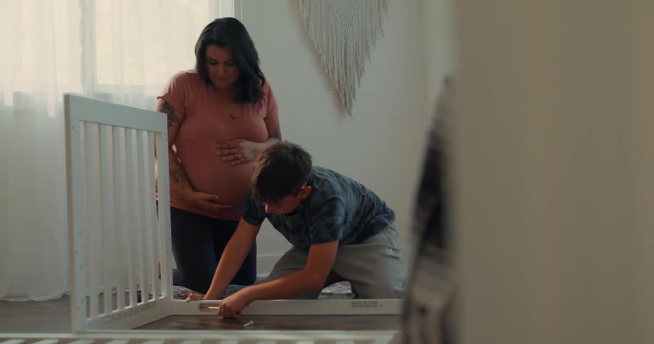 A mother watches her son build a crib
