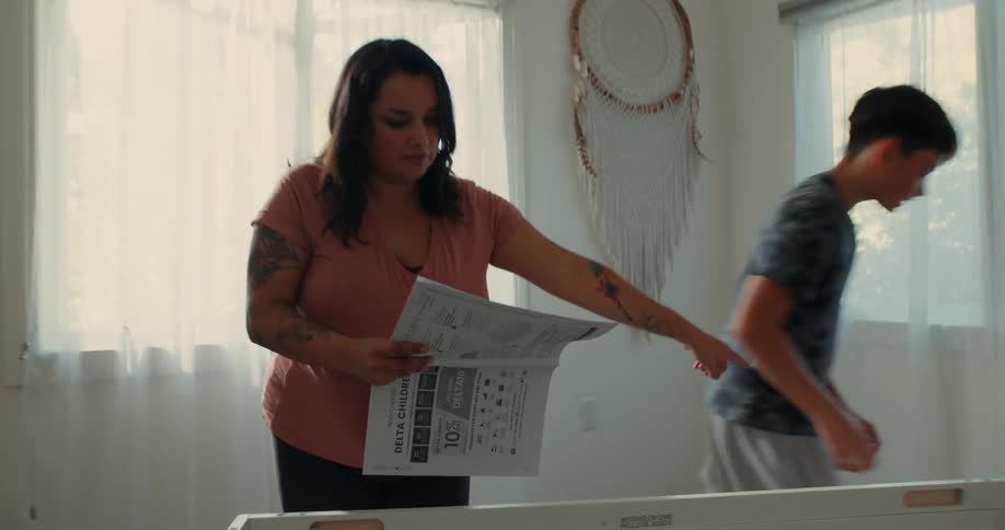 A mother reading instructions on how to assemble a crib points to a piece for her son to pick up