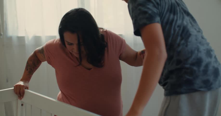 A son helps his pregnant mom get up off the ground near the crib in the room