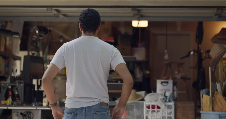 Garage door opening with boxes in storage and a man standing outside with his hands on his hips