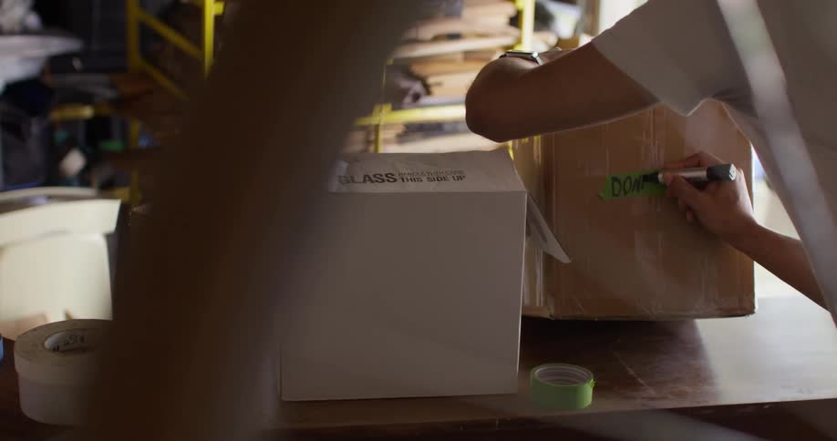 A person is labeling a cardboard box with a marker while in a cluttered garage