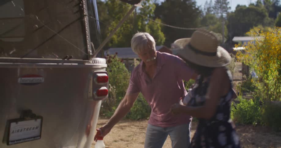 A couple walks toward and begins washing the back of their airstream trailer