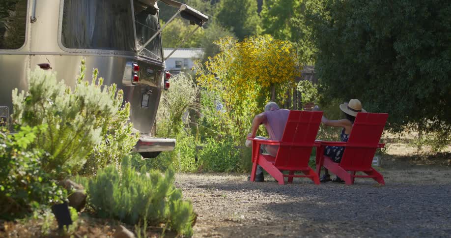 Couple cleaning two red chairs outdoors and sitting down