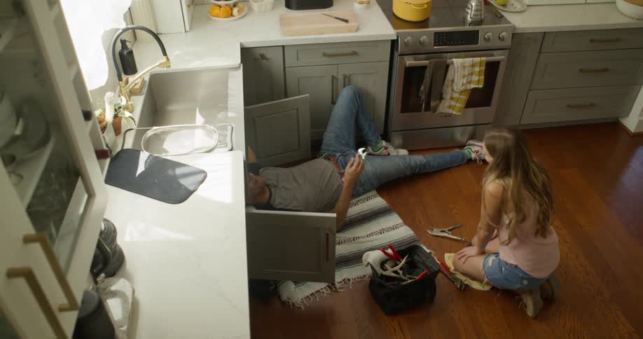 Woman handing a tool to a man who is fixing the kitchen sink