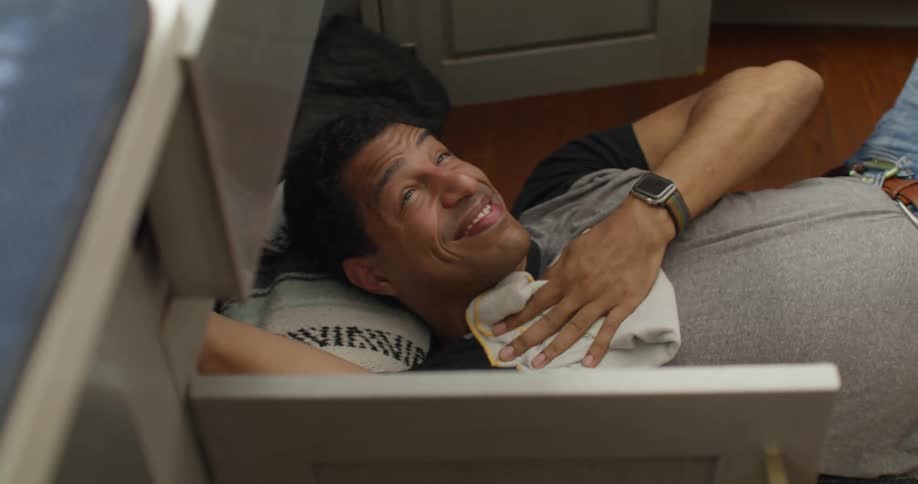 A woman hands a rag to a man fixing the sink
