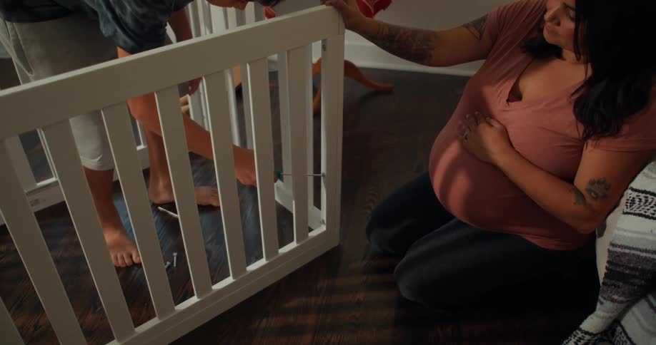 A mother kneels while watching her son build a crib
