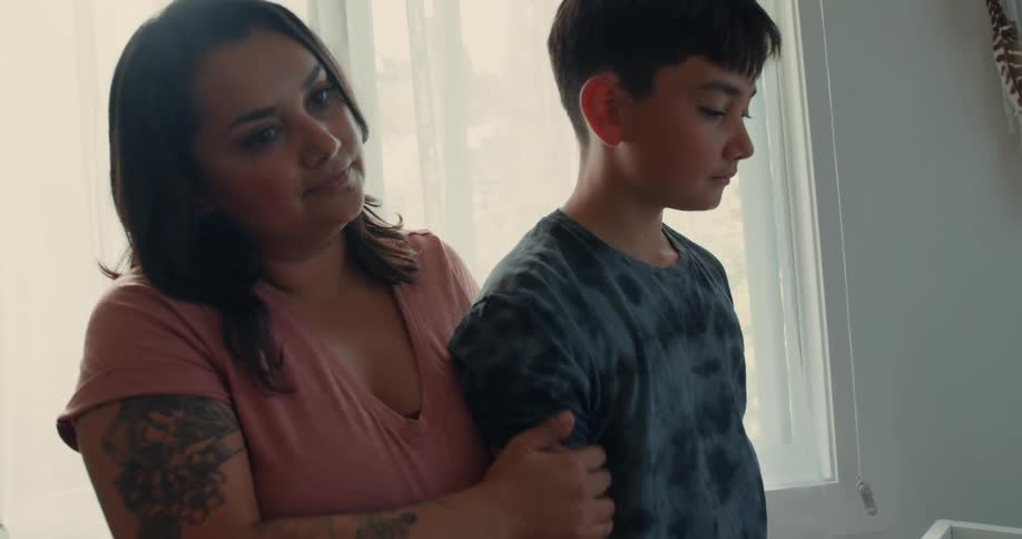 A pregnant woman is stroking the arm of a young boy who is looking at an empty crib