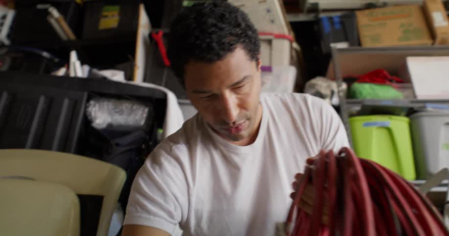 Man in a garage picking up a roll of red cable
