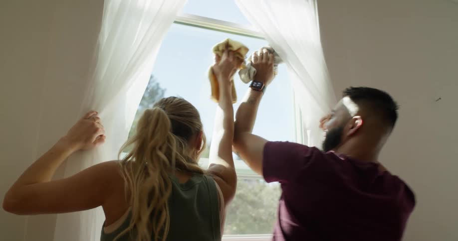 A man and woman play around while cleaning a window