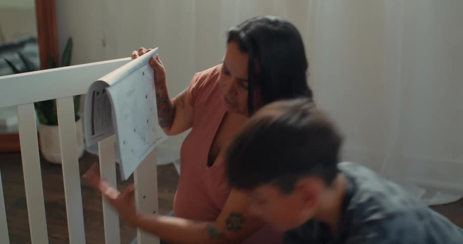 Pregnant mother looking at manual and a boy next to her assembling a crib