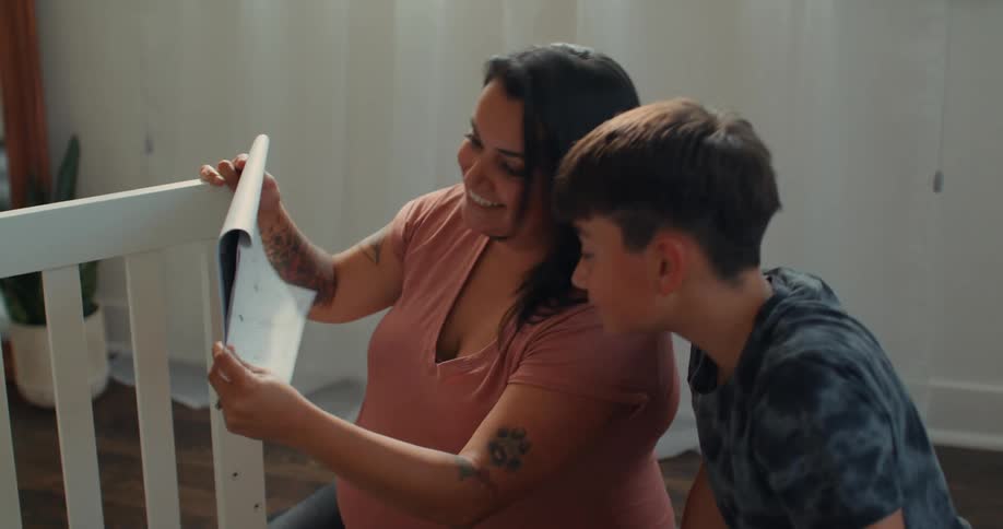 Pregnant mother sitting next to her baby looking at a manual for a crib