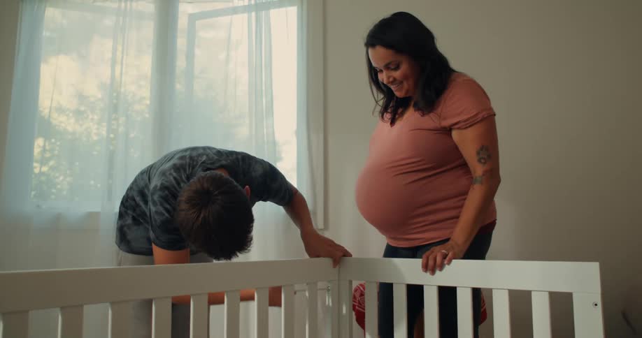 Teenage son assembling a crib for his very pregnant mother