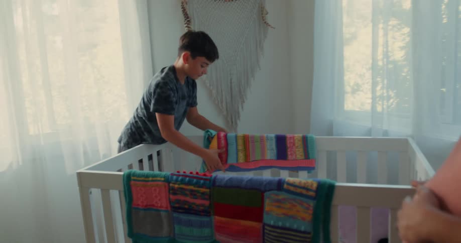 Pregnant mother in a room with a child placing a colorful cloth on the crib
